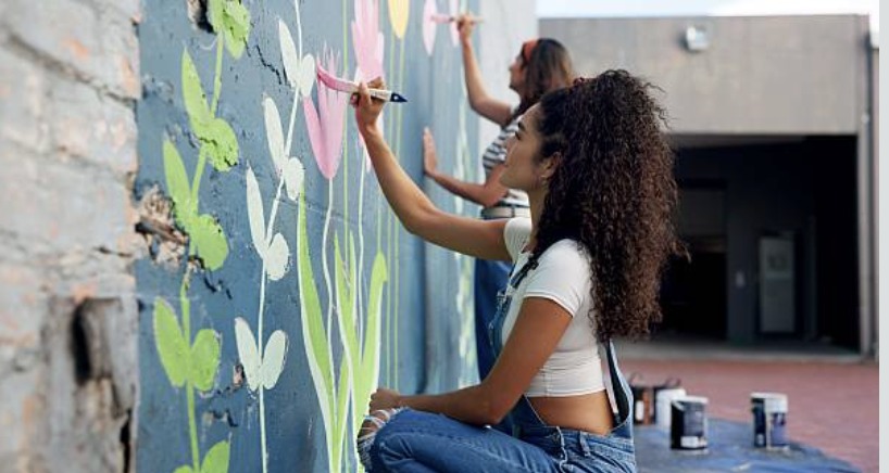 Two people painting a colorful floral mural on an outdoor wall